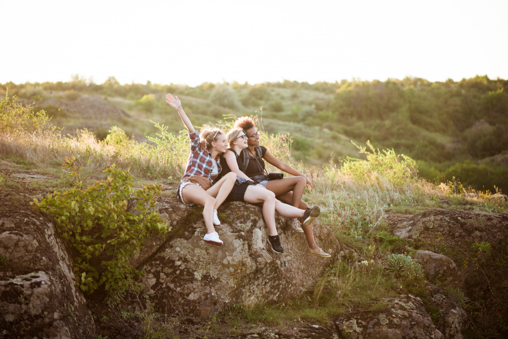 Three girls sitting next to each other on a hill and smiling