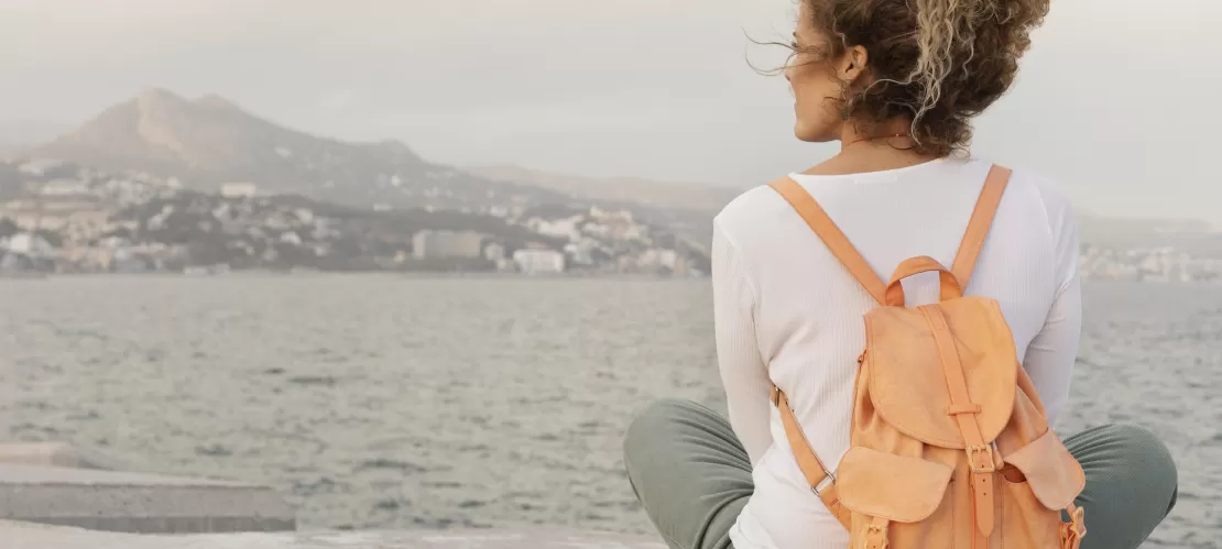 Full shot of a woman siiting on the offshore with backpack
