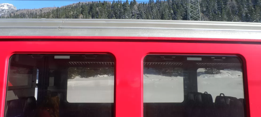 Red train passing through snowy landscape, viewed from outside