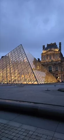 The glass Louvre Pyramid illuminated at night with historical buildings in the background.