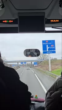 View from the front of a bus showing a blue road sign pointing toward Brussels.