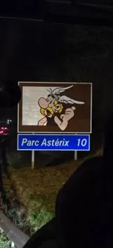 An illuminated road sign for Parc Astérix seen from a bus at night.