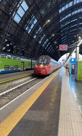 A red high speed train parked at a platform under the vaulted roof of the Milan train station.