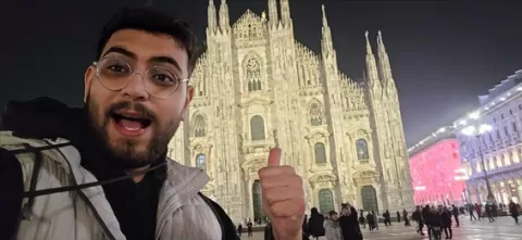 A nighttime selfie of me giving a thumbs up in front of the illuminated Milan Duomo cathedral.