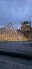 The glass Louvre Pyramid illuminated at night with historical buildings in the background.