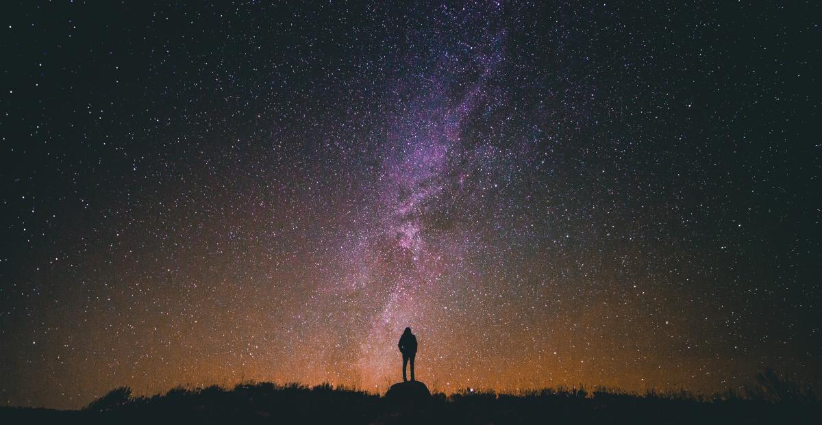 silhouette of man standing on rock while looking in sky