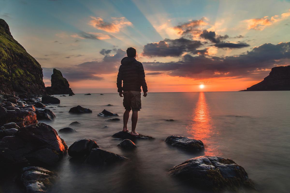 man standing on stone looking at sunset