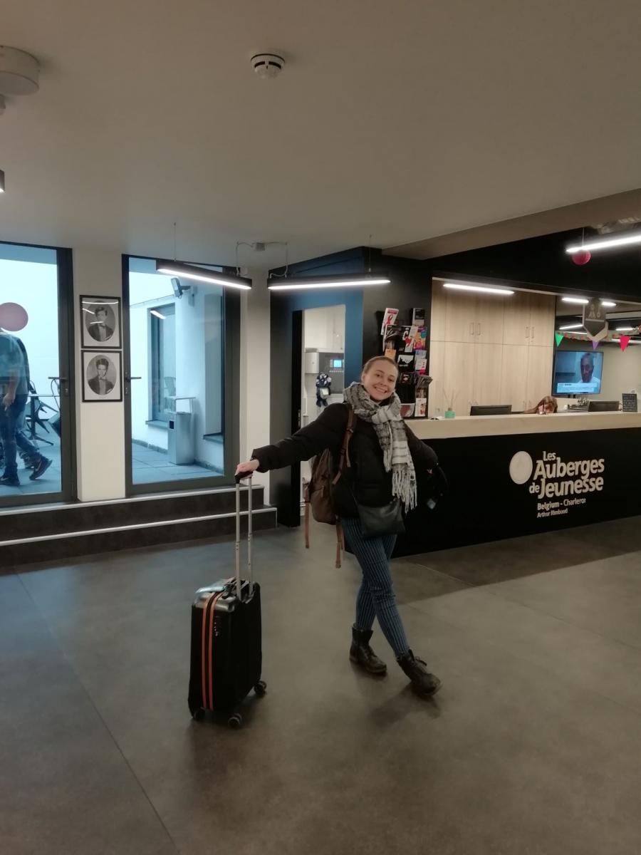 woman posing at the hostel entrance with suitcase