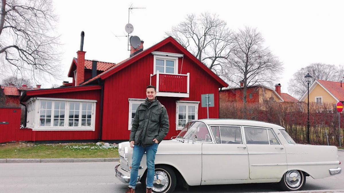 man next to car with red house in the back