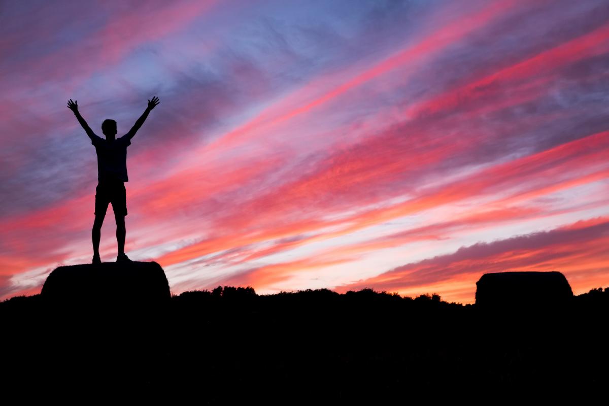 man with hands up and colourful sky