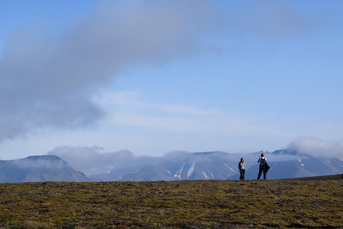 two people taking picture of the landscape, mountains in the background