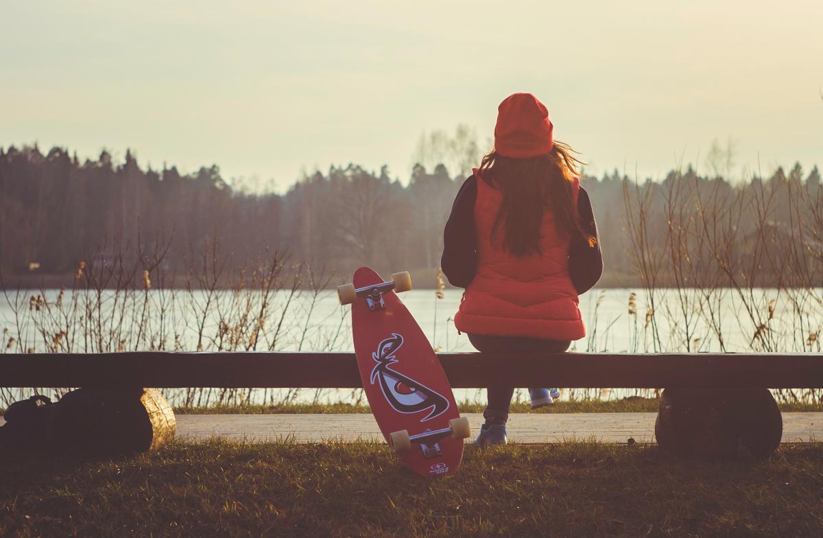 woman looking at lake with skateboard, from back