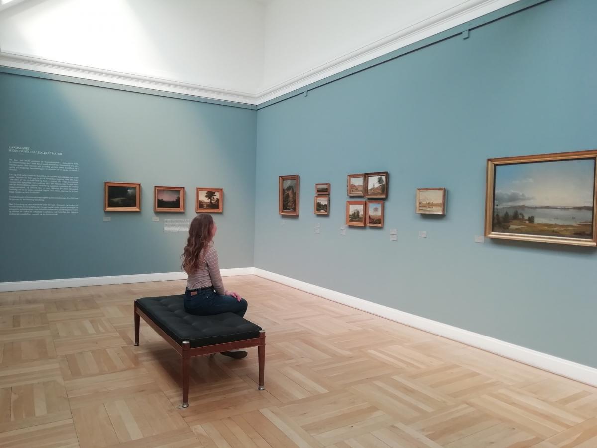 woman sitting at museum, watching paintings