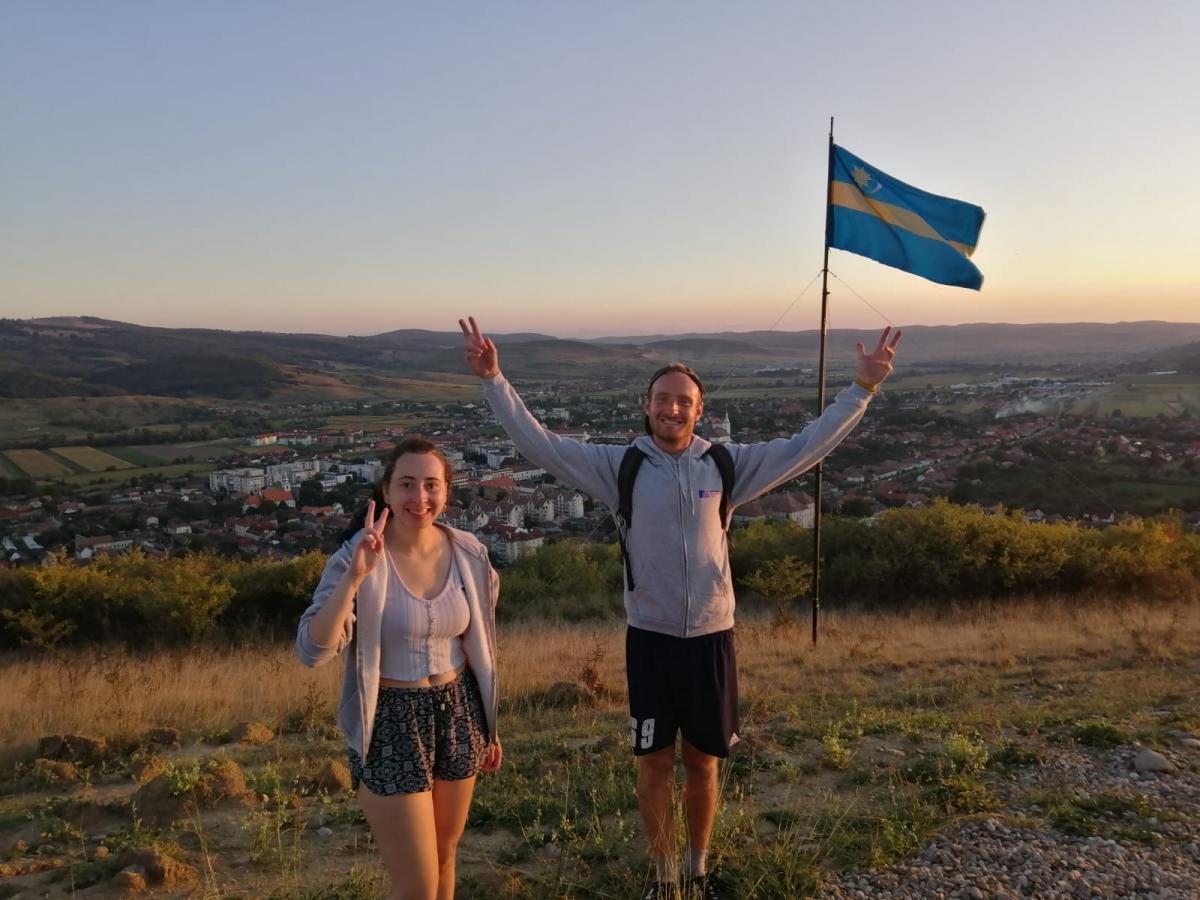 man and woman doing peace sign at top of hill with view on city