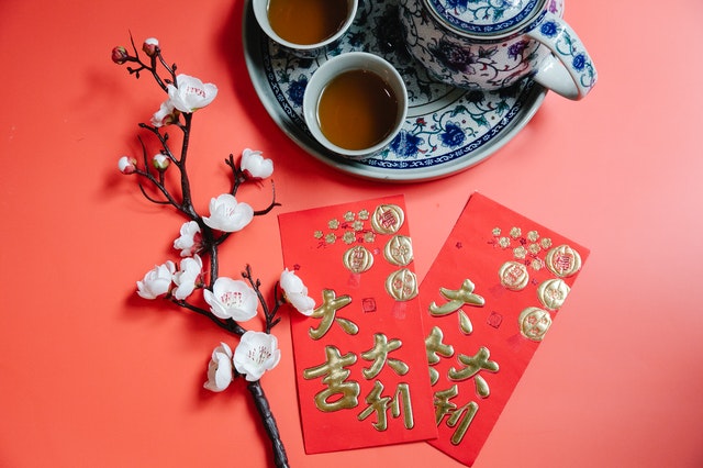 Red envelopes against sprig of blooming prunus and tea