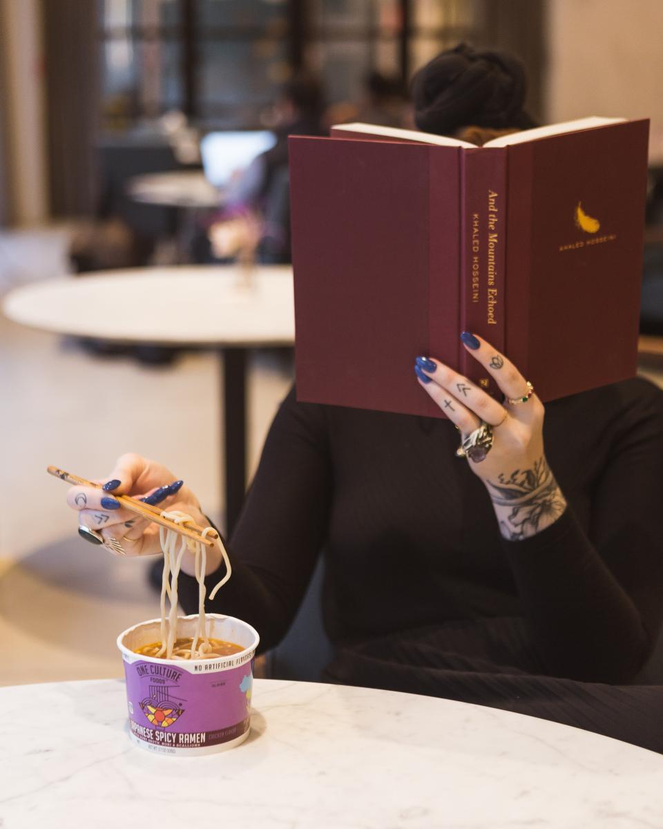 woman reading a book and eating noodles