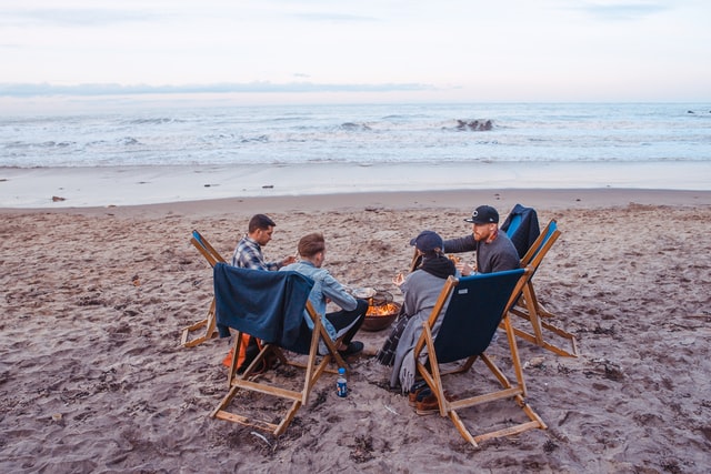 Three men and one woman sitting on beach lounge in front of fire pit