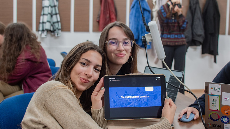 Two young girls showing the "We Are the Erasmus Generation" title on the tablet screen