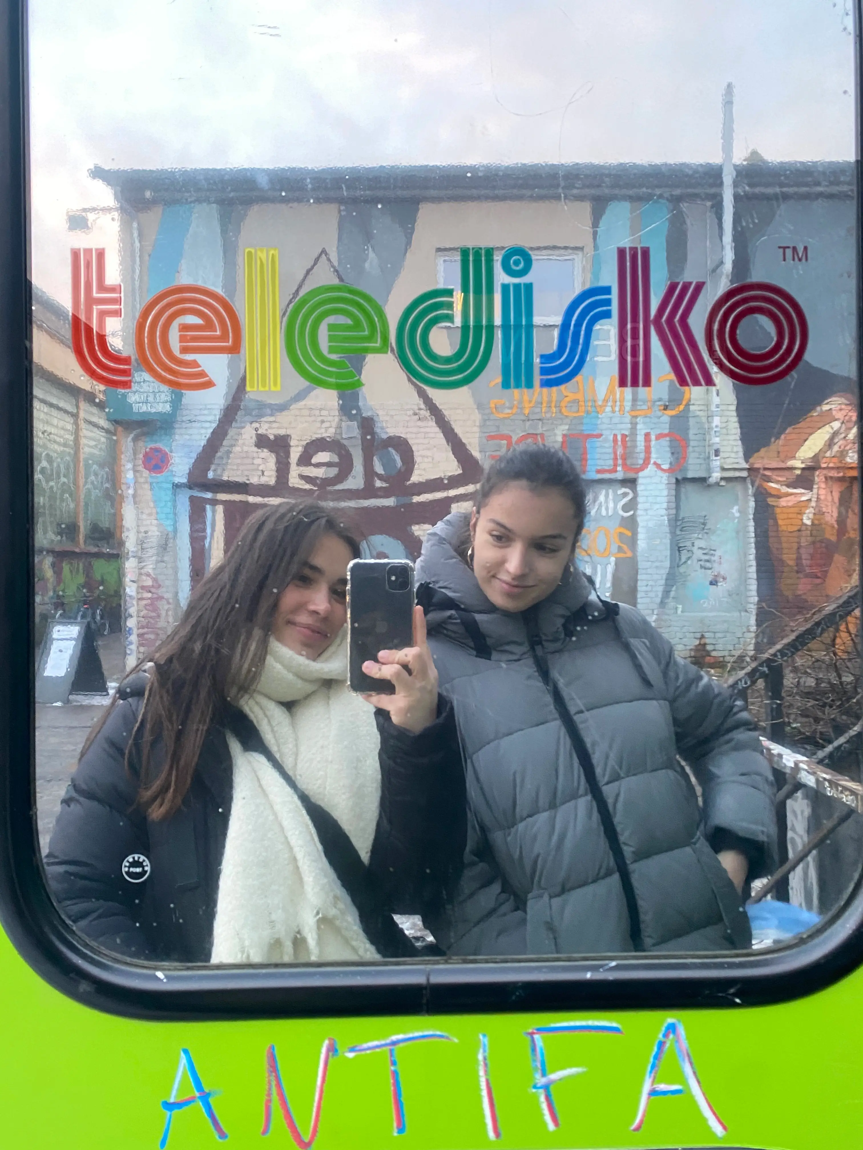Two girls taking a selfie in a mirror, in front of the Teledisco, Berlin