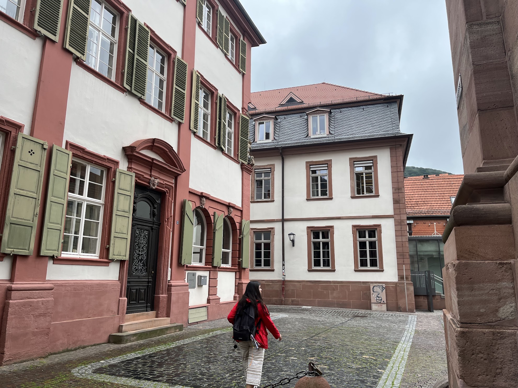 Altstadt - classical Heidelberg buildings have a red frame and white walls. Me walking in the middle of the photograph, with a red coat.
