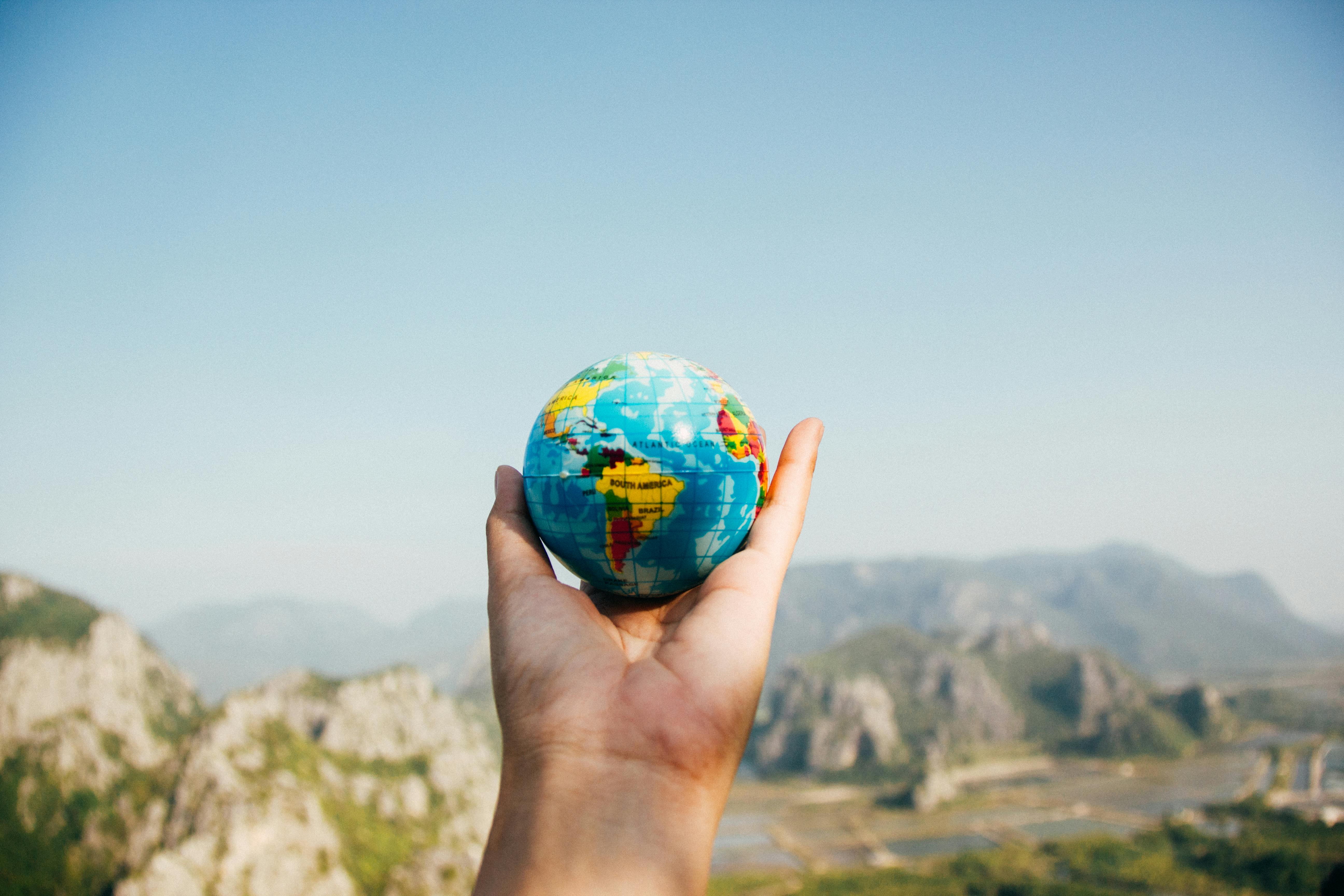 A person holding small world globe and facing mountain