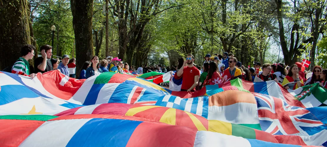 People standing around a big flag made out of different countires' flags