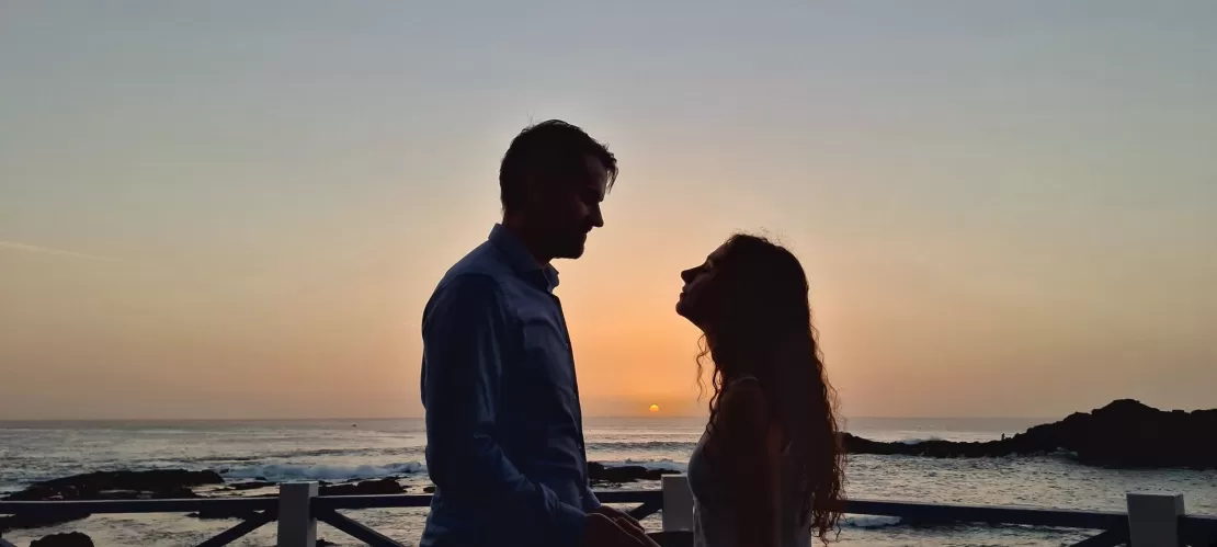 A view of twilight on the beach with a shadowed couple standing on the molo, the sea behind them.