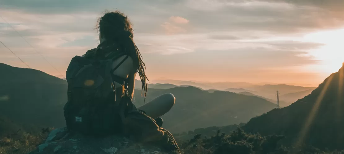 A young person sitting in surrounding of nature and watching the sun going down