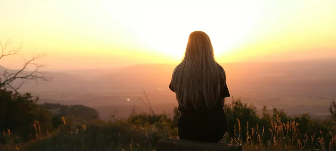 a girl sitting on a rock, surronded by nature and looking over the horizon