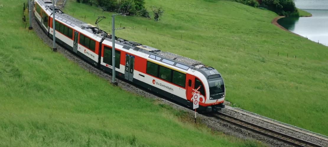 Swiss train going through the mountain countryside in front of a picturesque village and lake.