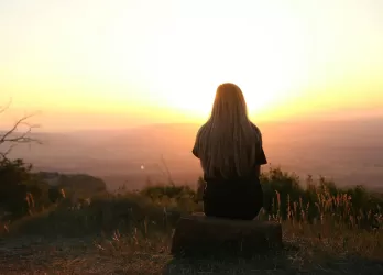 a girl sitting on a rock, surronded by nature and looking over the horizon