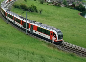 Swiss train going through the mountain countryside in front of a picturesque village and lake.