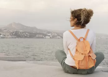 Full shot of a woman siiting on the offshore with backpack