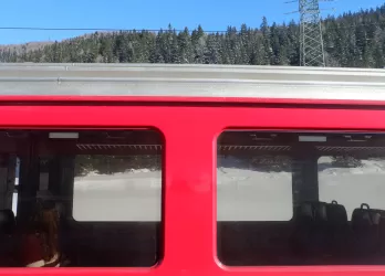 Red train passing through snowy landscape, viewed from outside