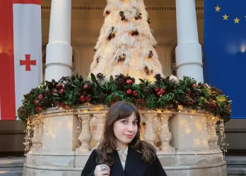 A brown-haired girl with flags of EU and Georgia in the background.