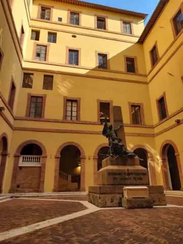 A yellow and orange building with a courtyard, where a statue of two men is situated. (Rectorate of the University of Siena)