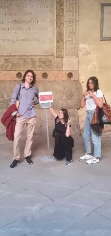 Three people next to a sign informing about elections. The person in the middle is squatting, the other two people are standing.