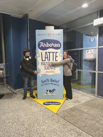 Two people, standing next to a giant milk carton, one of them hugging it