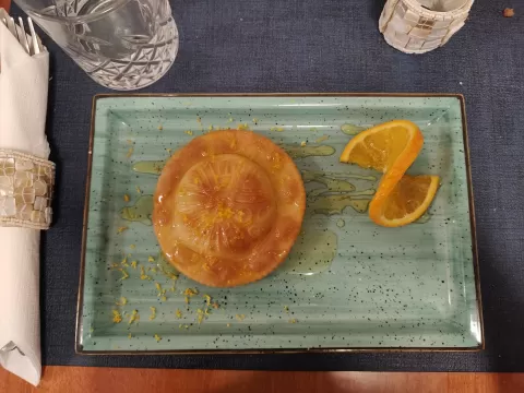 A pastry laying on a blue plate with an orange slice next to it